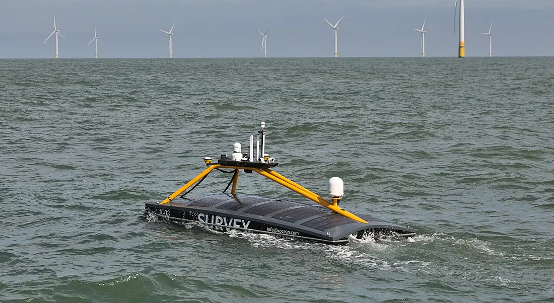 An Xocean unmanned surface vehicle with wind farms in the background.