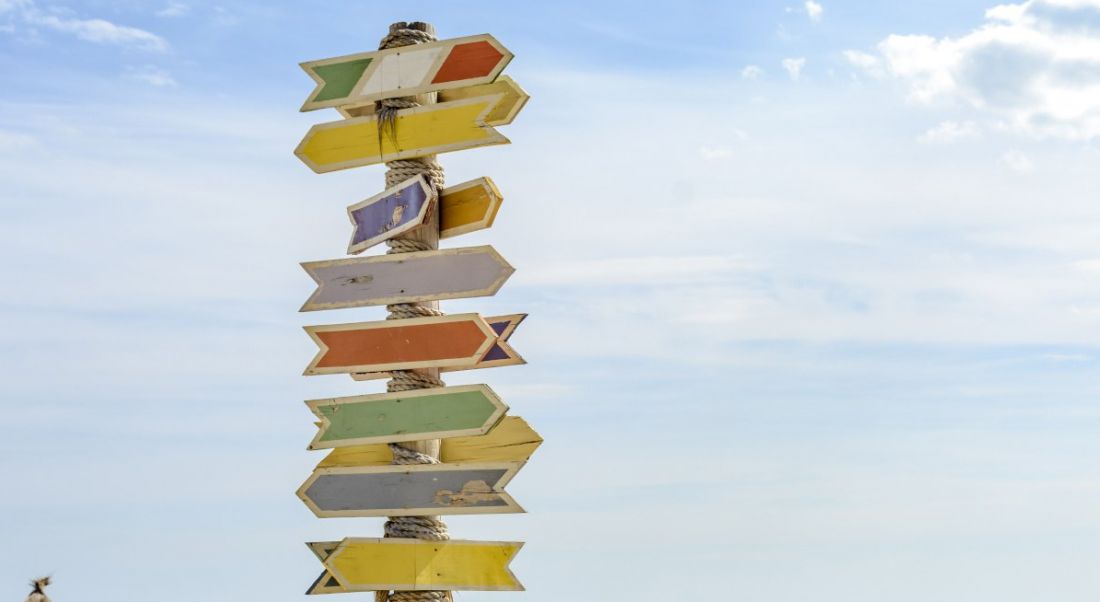 A tall pole with several different colour arrows on it pointing in different directions against a bright blue sky symbolising a career change.