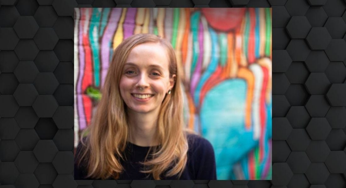 A woman with blonde hair smiles at the camera in front of a colourful graffiti wall.