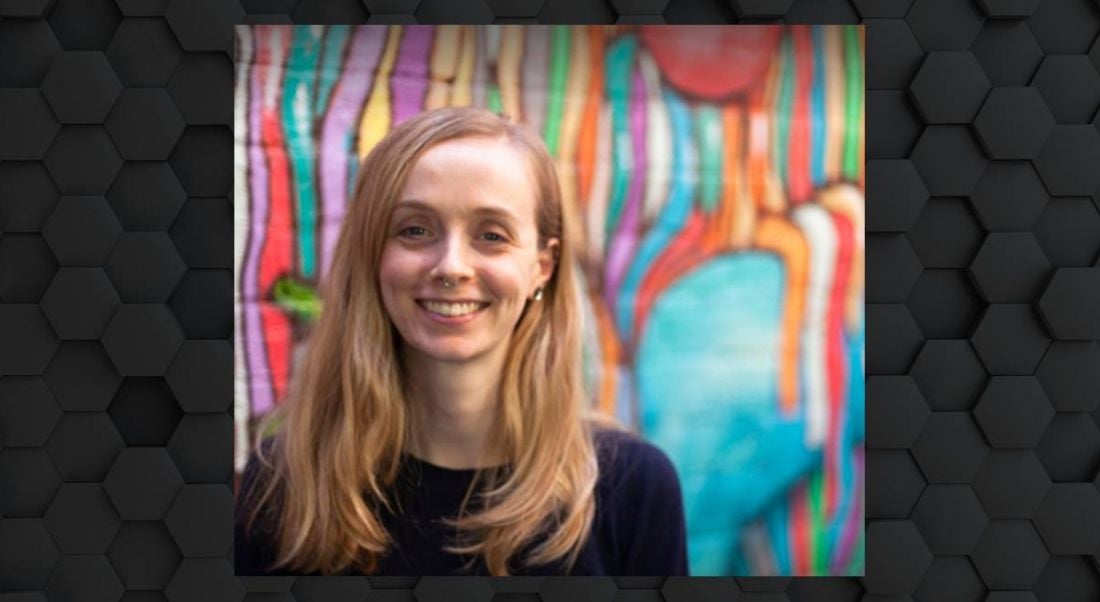 A woman with blonde hair smiles at the camera in front of a colourful graffiti wall.