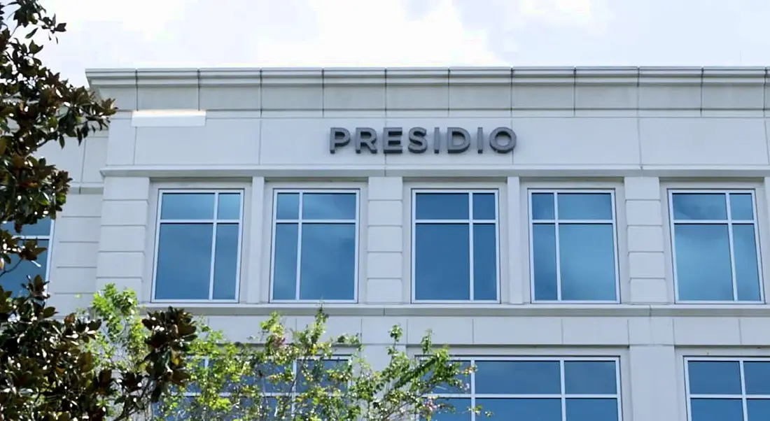 White building with Presidio logo on it. Partial trees visible on the left.