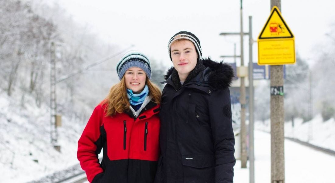 A woman and a man stand side by side beside a train track in the snow.