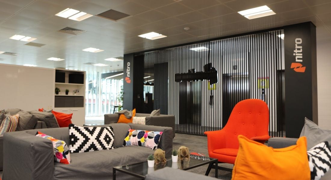 A modern office space at Nitro with grey couches and orange cushions.