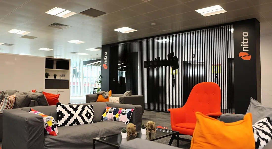 A modern office space at Nitro with grey couches and orange cushions.