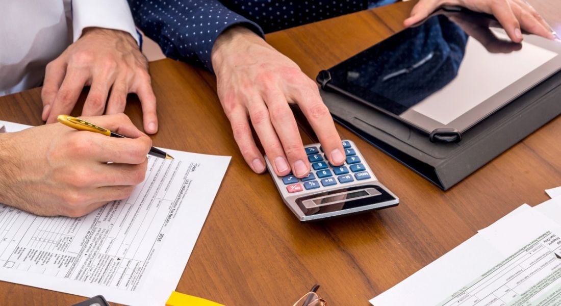 Two men working in financial services using a calculator as they assess financial documents.