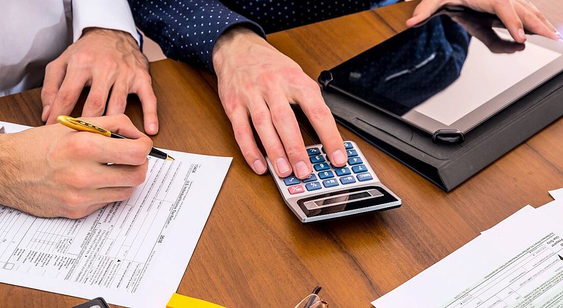 Two men working in financial services using a calculator as they assess financial documents.