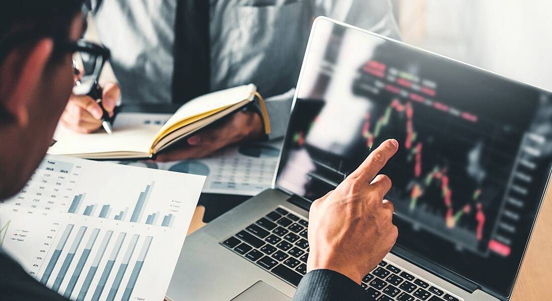 Businessman pointing to a computer showing a peak increase in a graph.