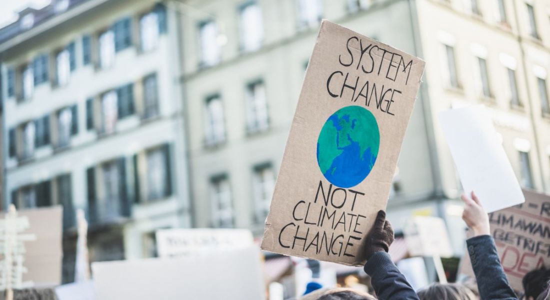 Group of climate action protestors holding a cardboard sign with a picture of the earth on it, protesting the climate crisis.