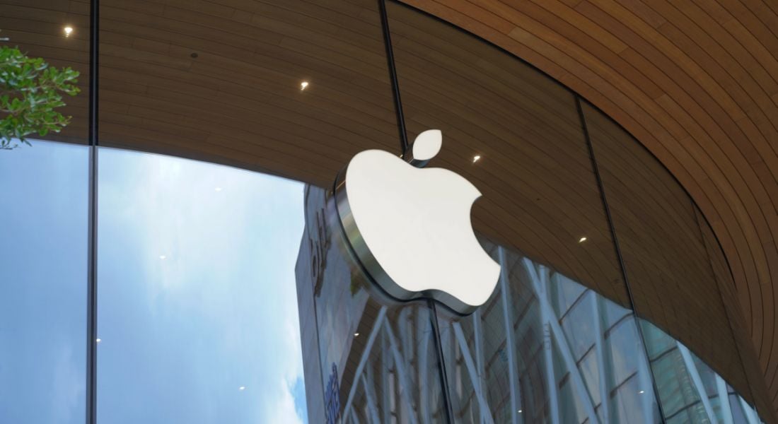 Apple company logo on a glass fronted building with foliage peeping into the frame on the left side.
