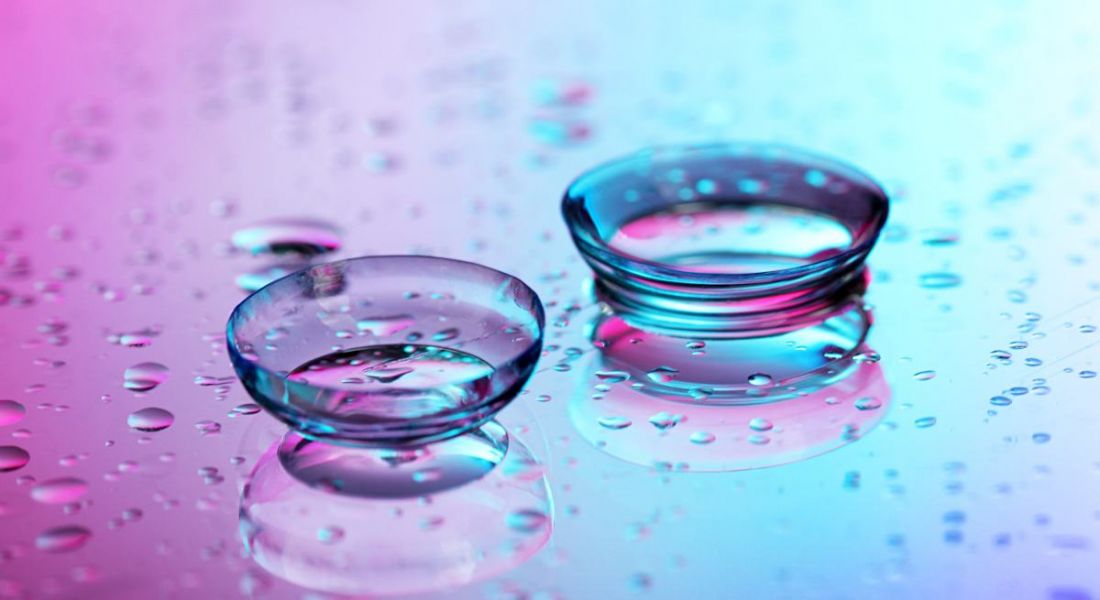 A pair of contact lenses flushed with water on a pinkish-blue background.