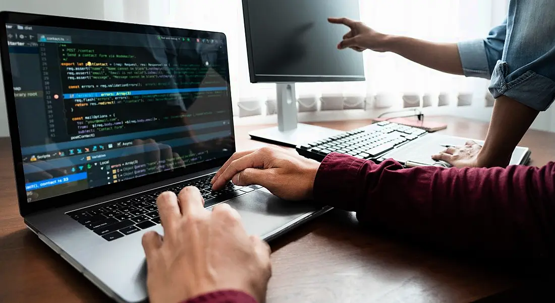 Two software developers' hands visible as they work on computers on coding programmes.