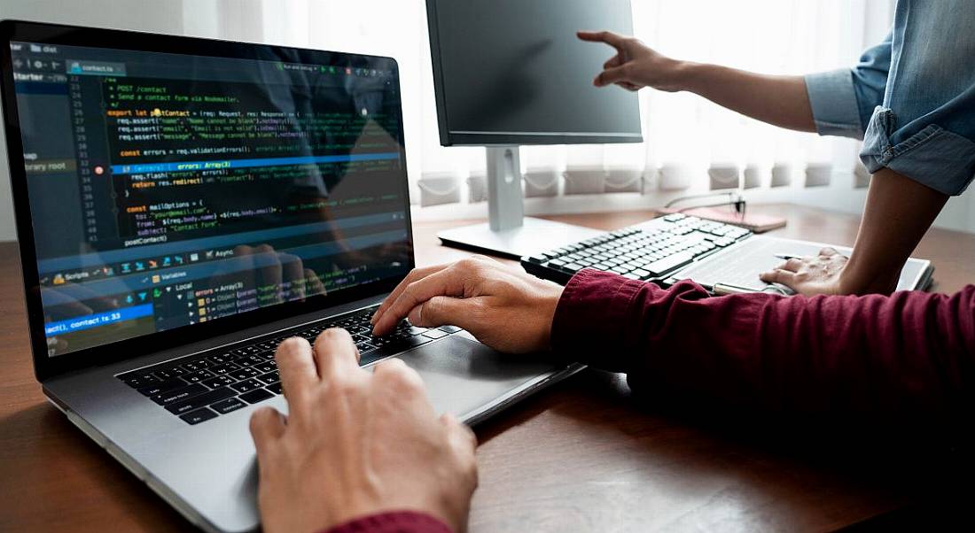 Two software developers' hands visible as they work on computers on coding programmes.