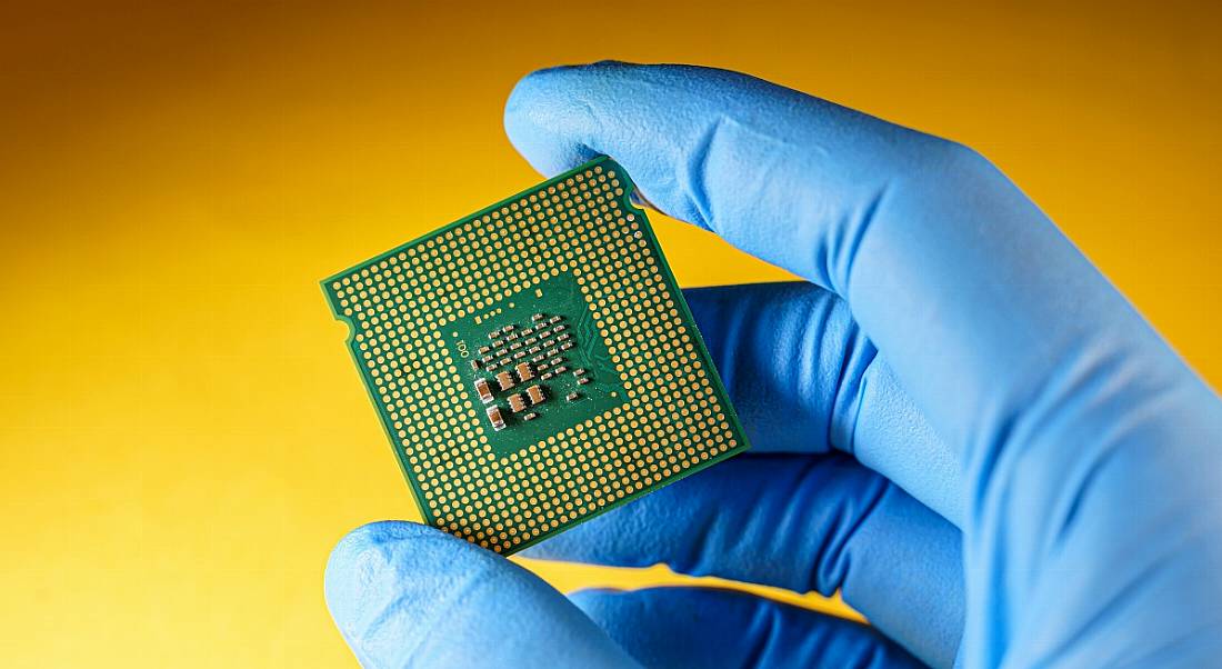 Blue gloved hand holding a semiconductor chip against a yellow background.