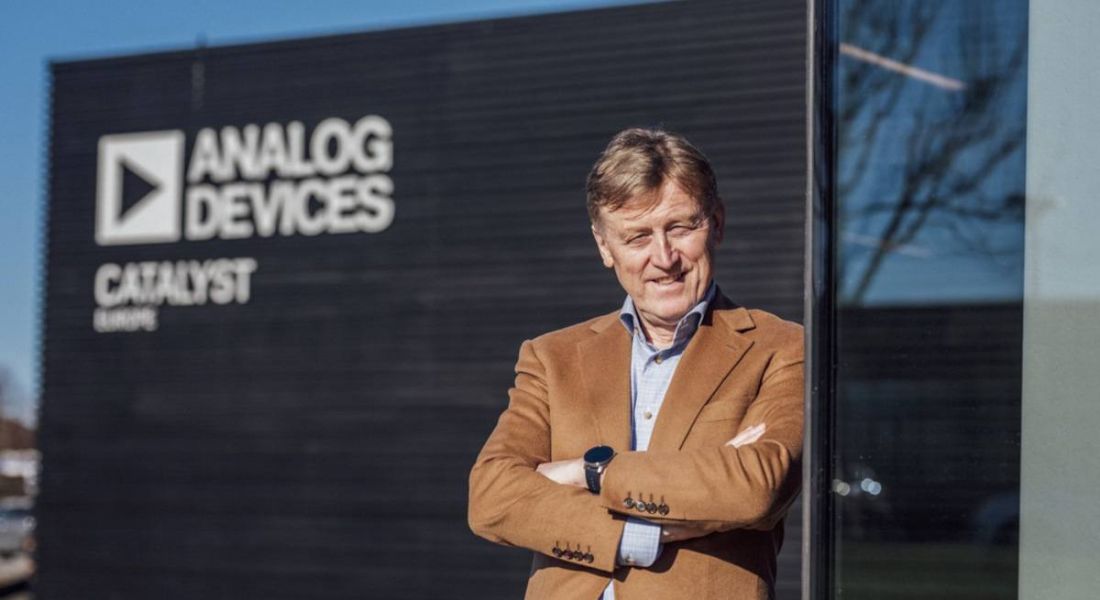 Vincent Roche CEO Analog Devices standing with arms folded outside one of its campuses which has the company's logo on it in white letters.
