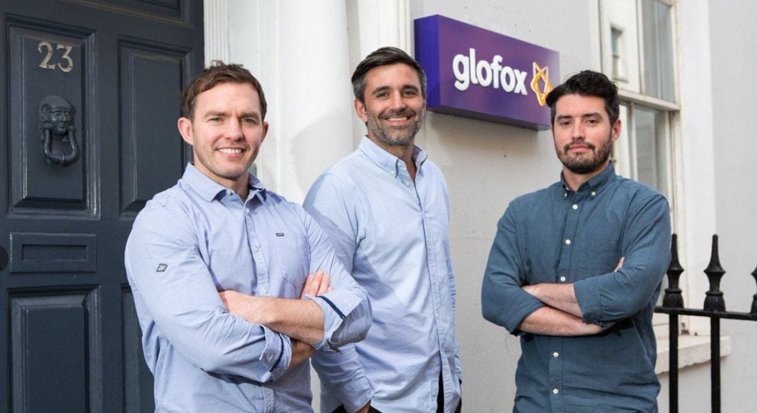 Three men stand outside the door to an office with the Glofox logo on the wall behind them.