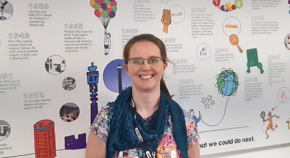 A woman smiling at the camera while standing in front of a wall that shows a timeline of the history of BT.