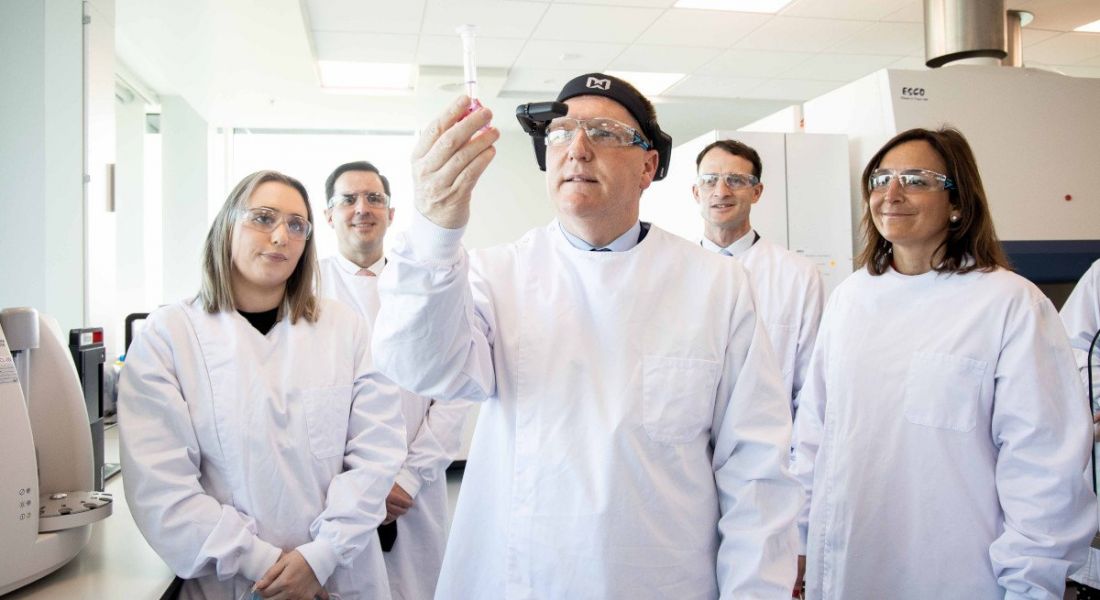 Five people stand in a lab wearing protective clothing, with TD Michael McGrath in the centre holding up a piece of equipment.