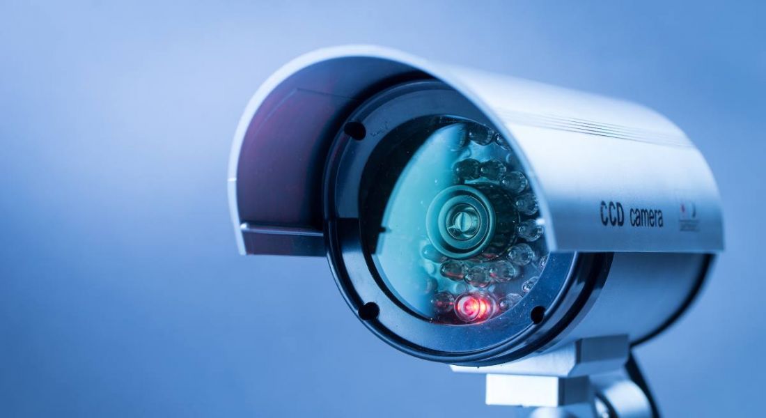 A close up of a security camera with a red light on it against a blue background.