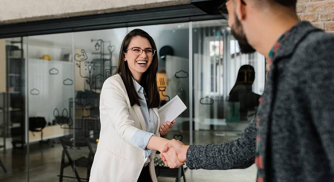 A woman shaking hands with a man and smiling. It’s her first day back working for a former employer.