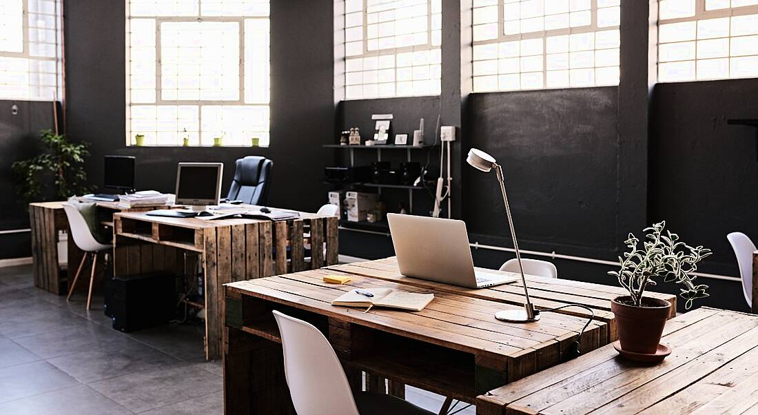 A contemporary office space with black walls, bright windows and wooden crate-box desks.