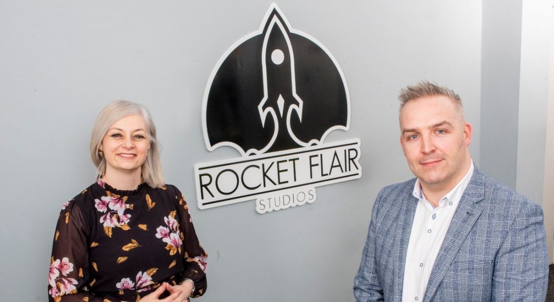 Susan O'Kane and James Bradley standing in front of a Rocket Flair Studios logo.
