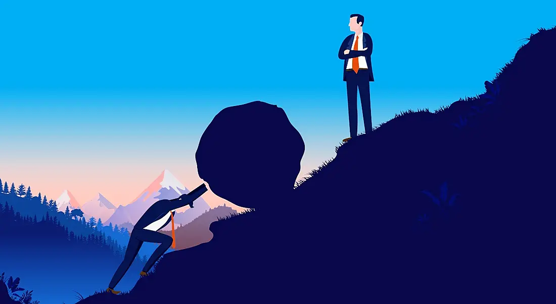 A cartoon image of a man in a suit pushing a boulder up a hill while another man stands higher up the hill staring at him. Representing a struggling employee.