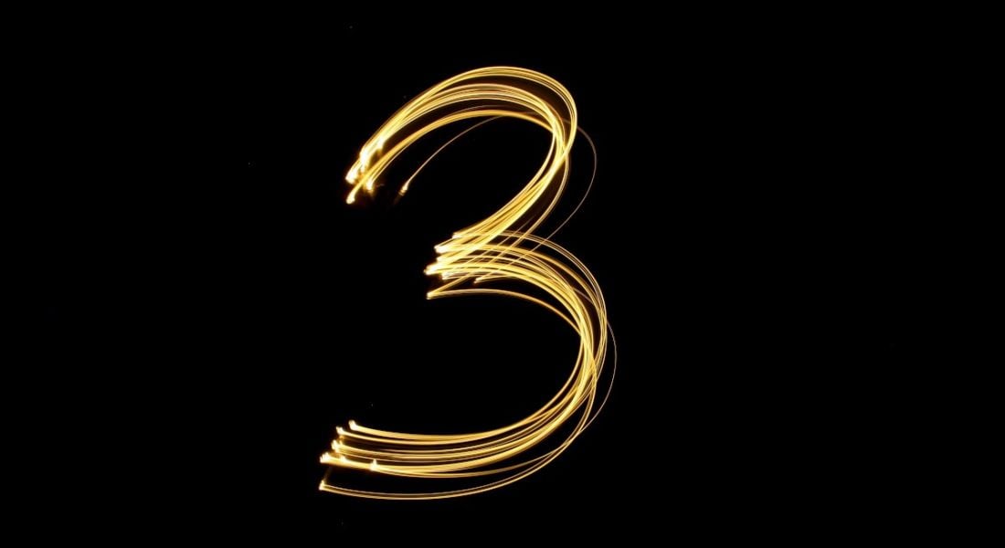 A long exposure shot of gold lights drawing out the number three against a black background.