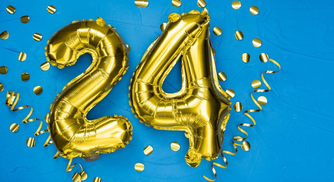 Two gold foil balloons that spell out the number 24 against a blue background.