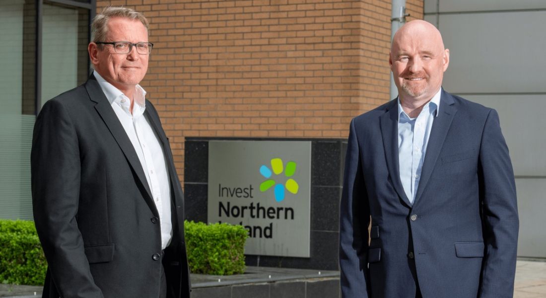 Two men standing outside a red brick building with an Invest NI sign.