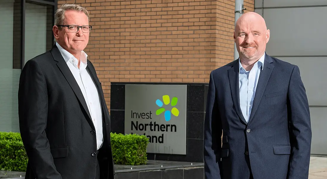 Two men standing outside a red brick building with an Invest NI sign.