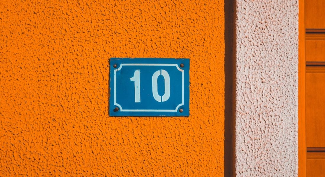 A number 10 house sign on a bright orange wall.