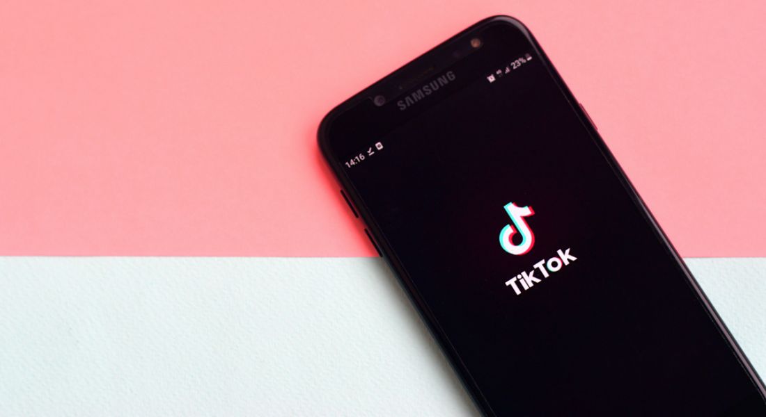 A phone is lying against a graphic background, with the TikTok logo on the screen.