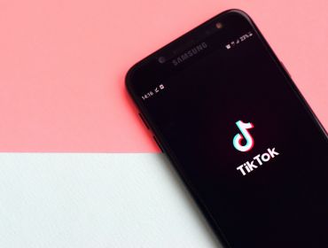 A phone is lying against a graphic background, with the TikTok logo on the screen.