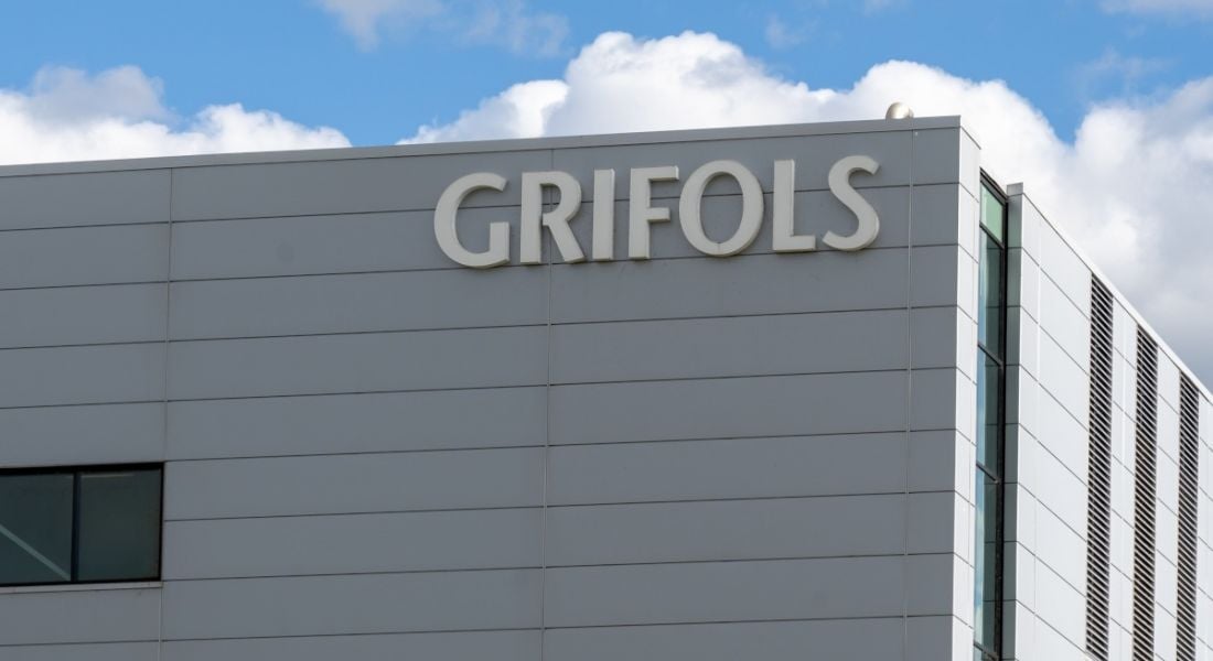 The corner of a large white building with Grifols logo on it.