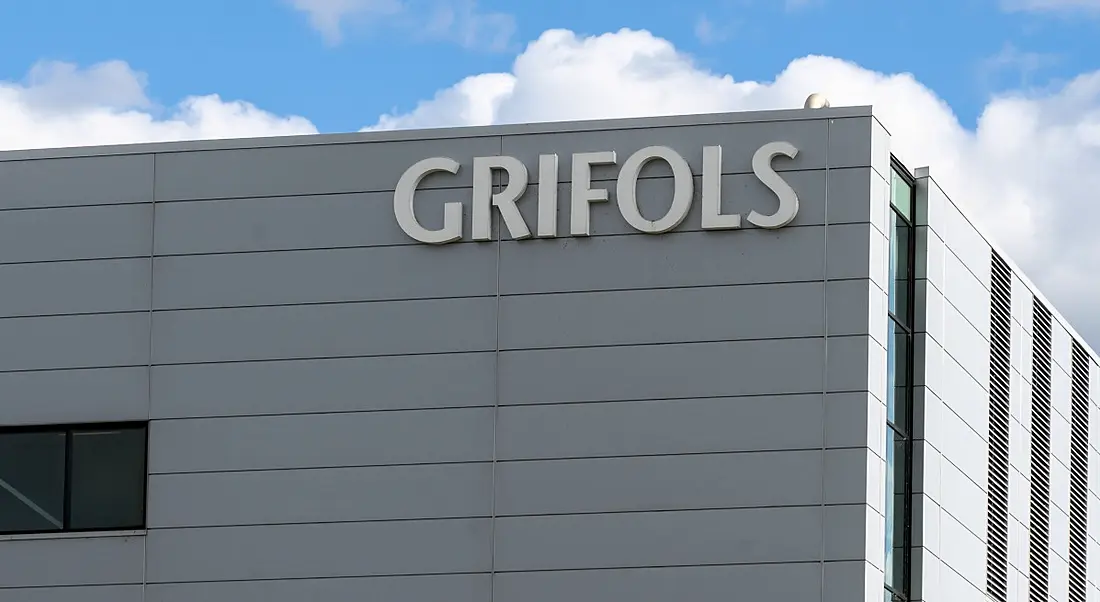 The corner of a large white building with Grifols logo on it.