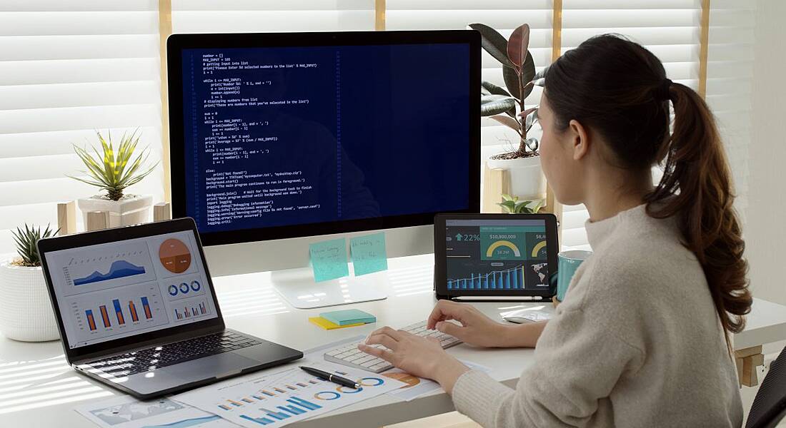 Woman sitting in front of a computer and laptops working in tech.