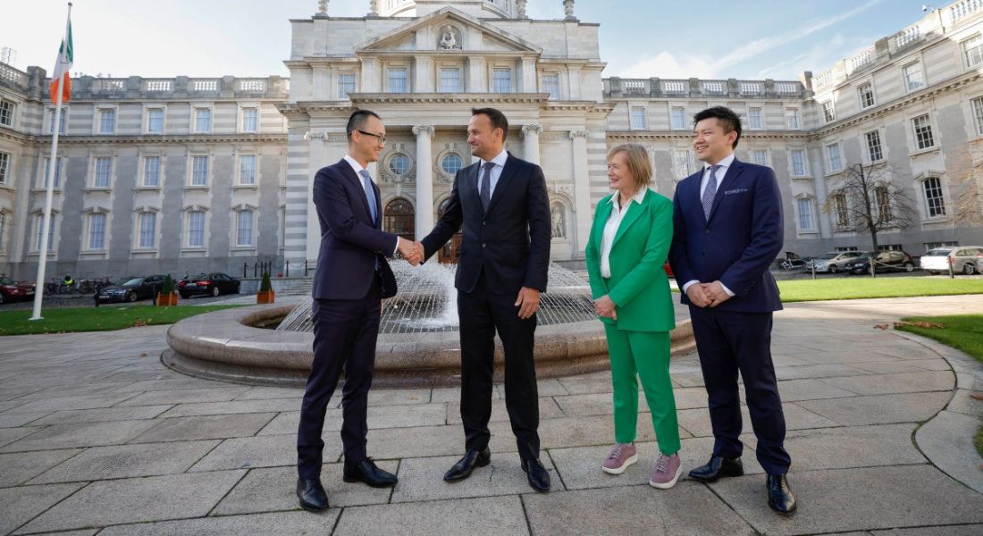 Three men and a woman standing in front of a large building, with two of the men shaking hands. They are members of Huawei, the Irish Government and IDA Ireland.