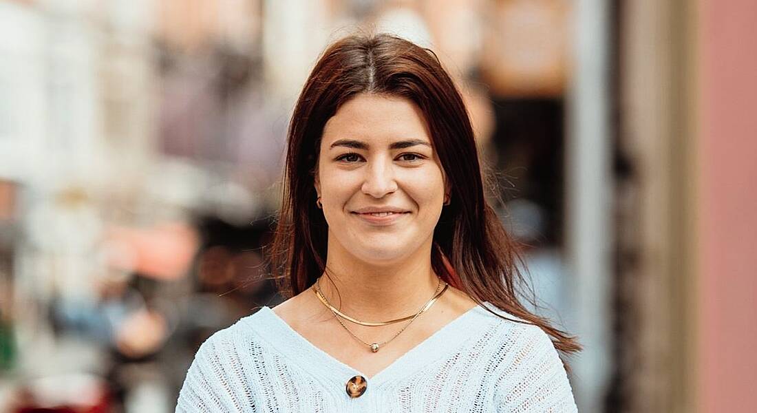 A young woman wearing a blue cardigan smiles at the camera.