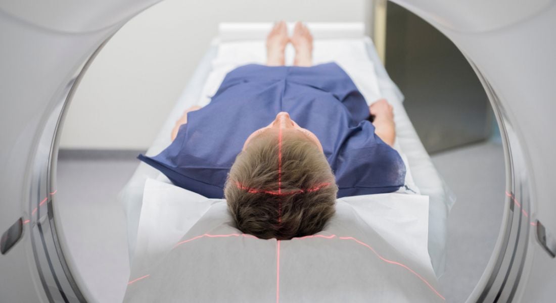 A person wearing a blue patient robe lying in a CT scanner.