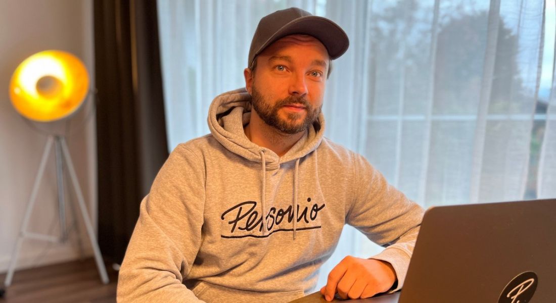 Stephan Lengl, Personio engineer, sitting in a room at a desk with a computer wearing a Personio branded hoodie.