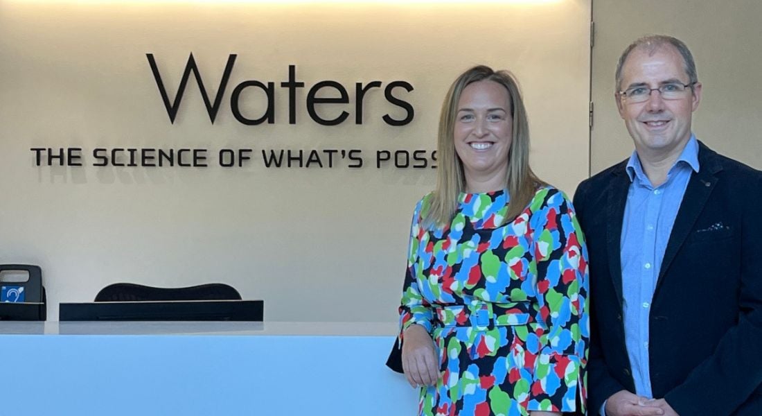 A woman and a man standing in front of a Waters company logo in a building.