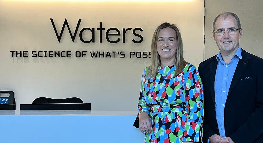 A woman and a man standing in front of a Waters company logo in a building.