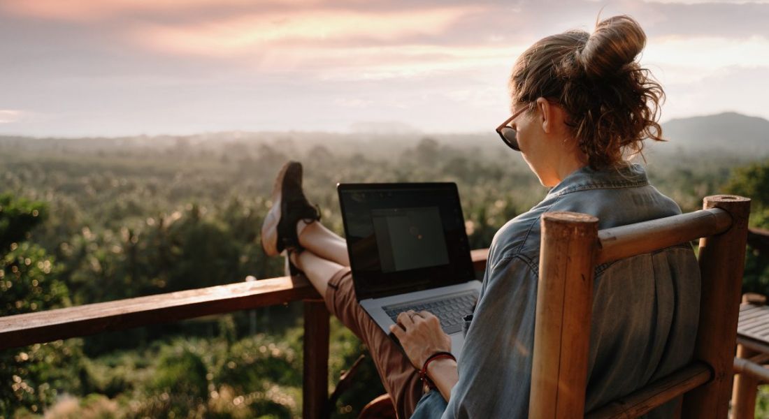 A woman with a computer on her lap working remotely. Scenic view in front of her.