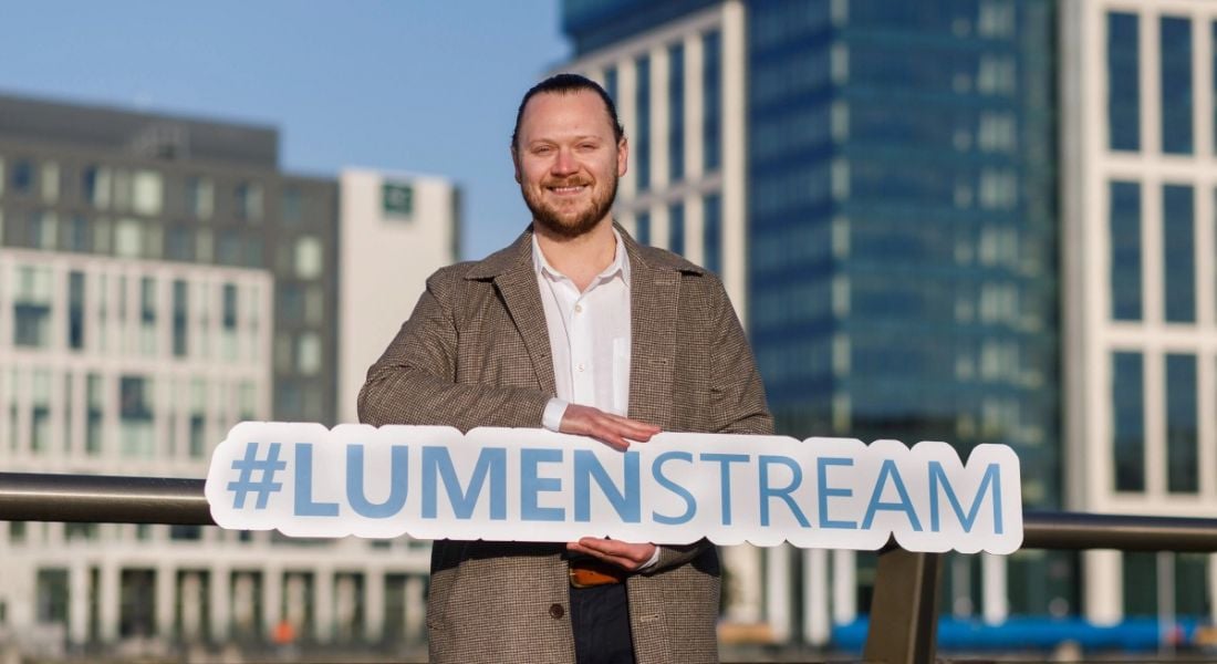 Alistair Brown, CEO and founder of Lumenstream, standing outside with buildings in the background. He is holding a Lumenstream sign.