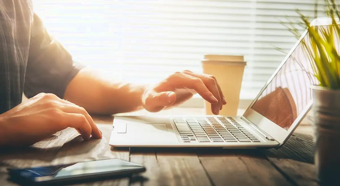 A person’s hands working on a laptop in a brightly lit room.