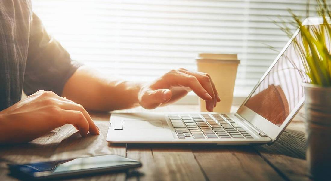 A person’s hands working on a laptop in a brightly lit room.