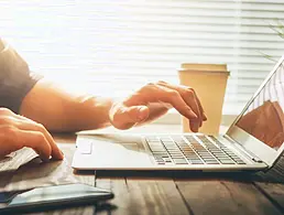 A woman at work is sitting, smiling at her laptop.