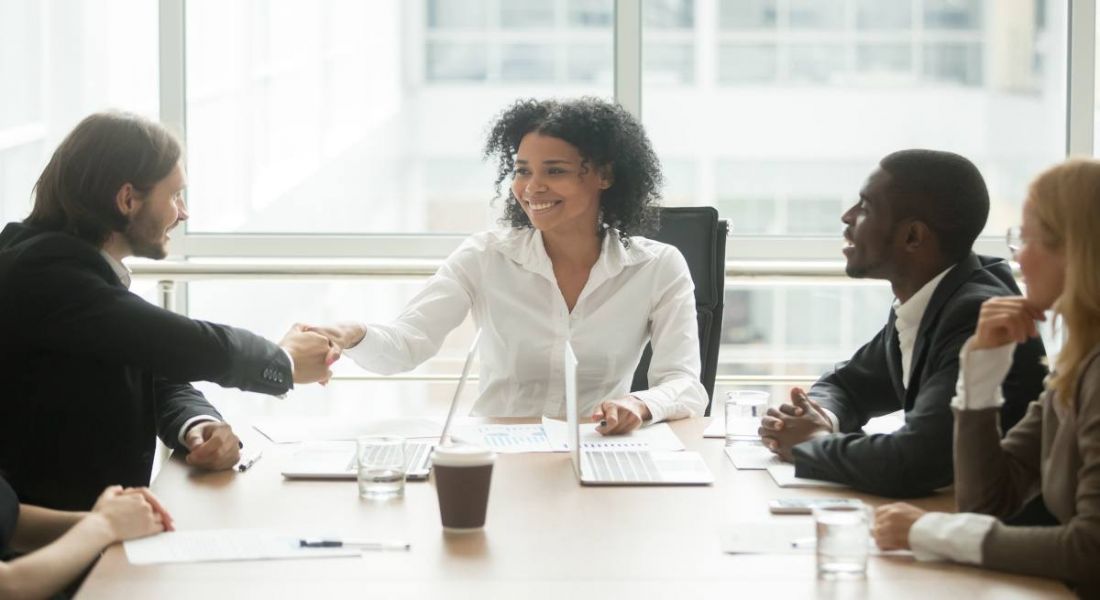 Woman shaking man's hand in a workplace setting while two other employees look on.