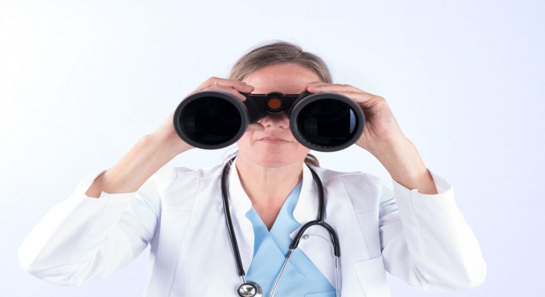 A person in a lab coat looks through a pair of binoculars.