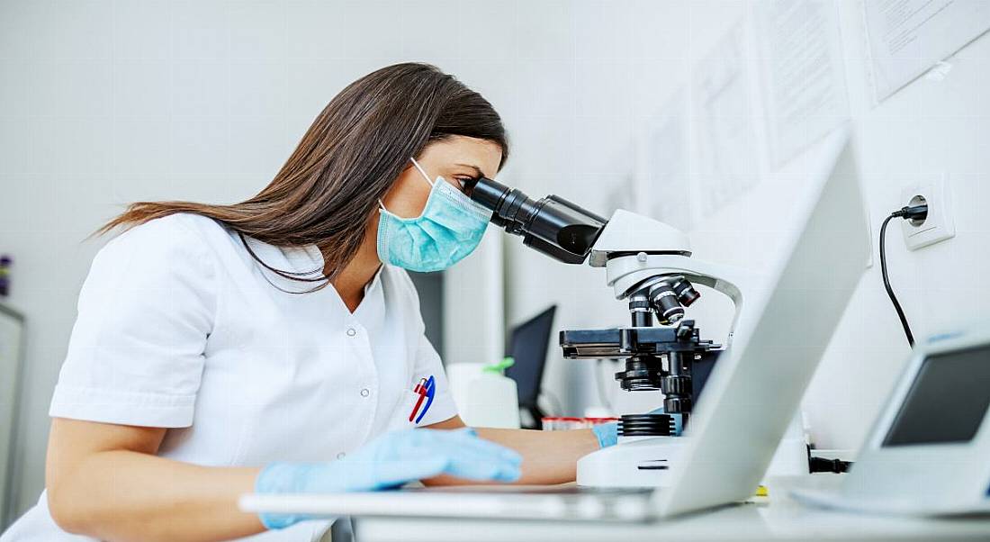 Woman working in a biomedical laboratory using a microscope.